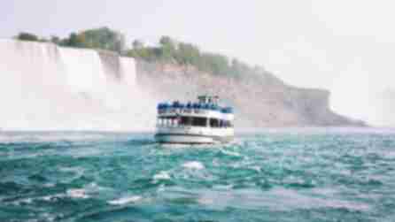 People in blue ponchos stand on the top deck of the Maid of the Mist boat tour as it passes by Niagara Falls
