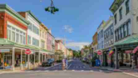 Two people crossing the street in the historic Stockade District of Kingston where a Pride flag flies from a corner light post.