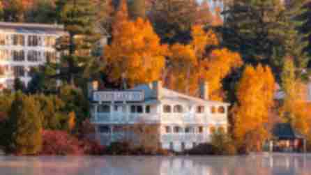 A white Inn sitting next to a lake surrounded by the bright orange leaves of fall