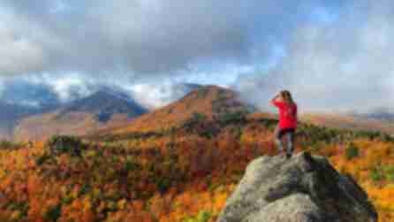 A person in red looks out at sprawling fall foliage throughout the Adirondack High Peaks