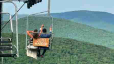 A bride and groom sit on a ski lift that reads "Just Married" on the back while looking out over the Catskill Mountains