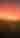 A barn sits in a field beneath a red night sky full of stars.