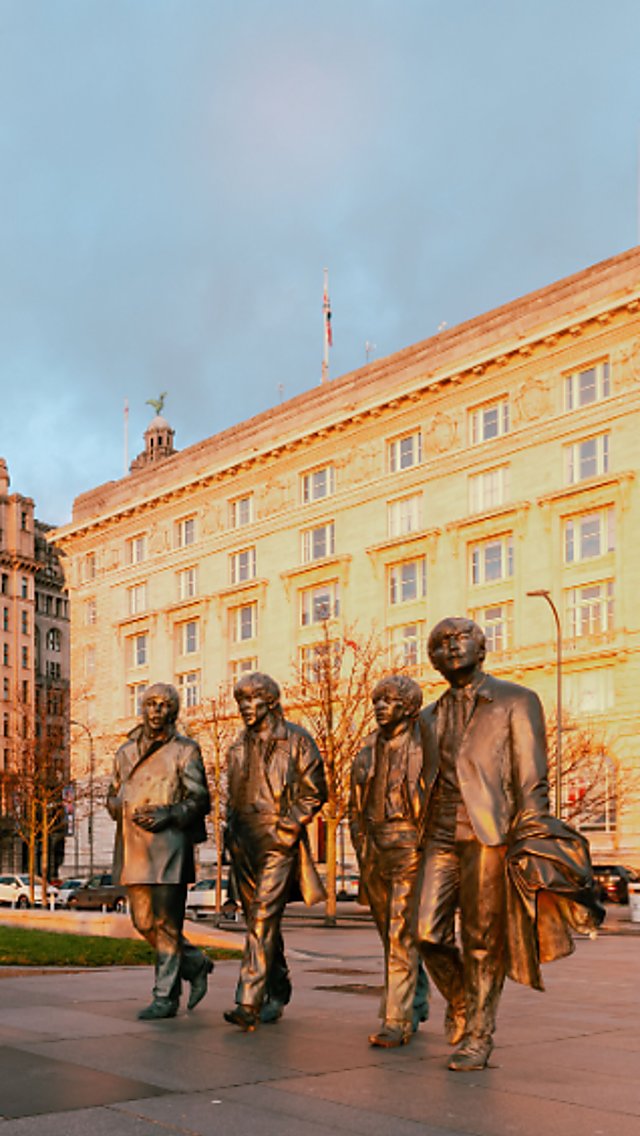 The Beatles statue with the Royal Liver building in the background, with the sun setting on the Cunard building.