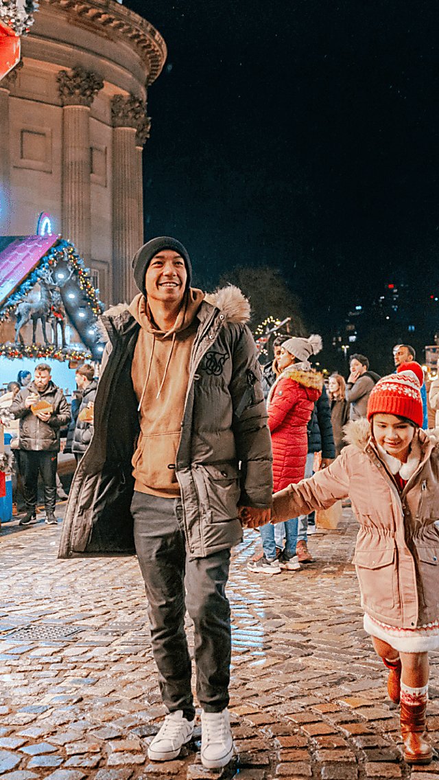 Two people holding a child's hand with the Liverpool Christmas market behind them.
