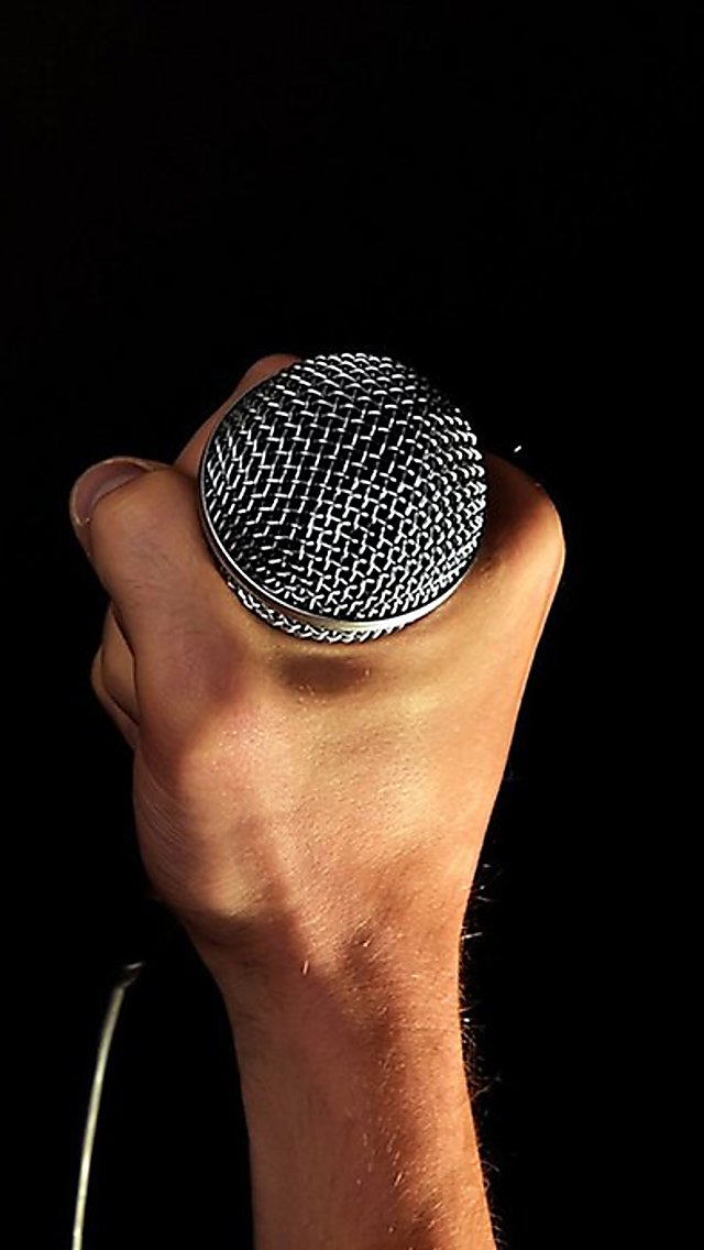 A hand holding a stand up microphone with a black background.