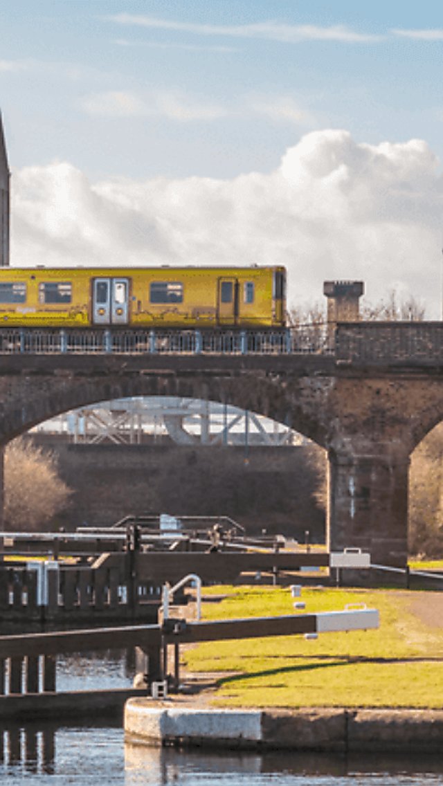 A yellow train pictured along a brick railway bridge running above a canal lock system.