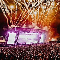 A large stage on Liverpool's Pier Head with fireworks coming from the top of it and a large crowd of people.