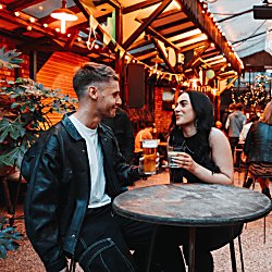 A male and female sit at a table in an outdoor, upcycled style bar.