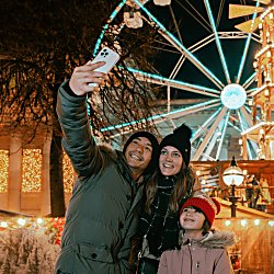 A couple taking a selfie in front of a large ferris wheel at the Liverpool Christmas Market