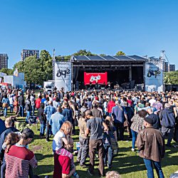 People in Sefton Park in the sunshine surrounding a stage