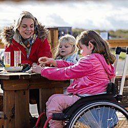 A family sit at a table and chairs outside, one of the children is in a wheelchair