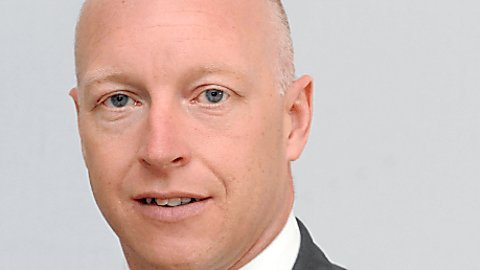 A man looking at the camera and wearing a red tie with a grey blazer and white shirt.