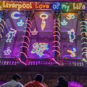 People standing outside Liverpool Town Hall which is decorated in neon lights