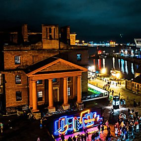 Part of the royal albert dock at night with a light installation on the front.