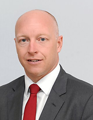 A man looking at the camera and wearing a red tie with a grey blazer and white shirt.
