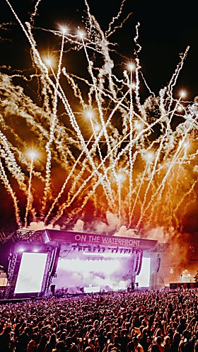 A large stage on Liverpool's Pier Head with fireworks coming from the top of it and a large crowd of people.