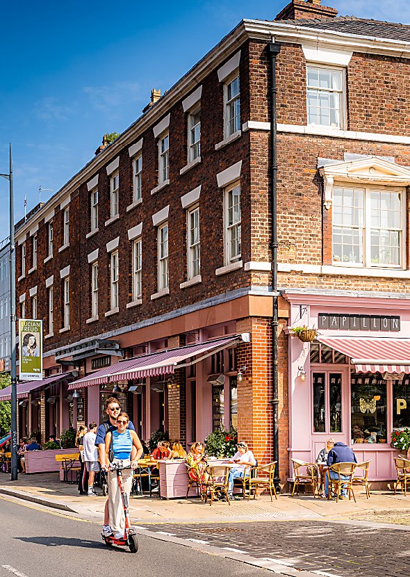 Two people on a Voi Scooter in the Georgian Quarter on a sunny day