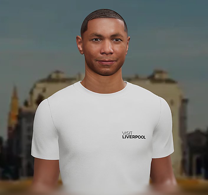 A centered, front-facing portrait of a person wearing a plain white T-shirt with the words “Visit Liverpool” printed in small black text on the upper left chest. The background is softly blurred, showing indistinct buildings and architectural shapes, giving a city setting. The person is framed from the chest up, with even lighting and a neutral backdrop that keeps focus on the face and the shirt’s text.