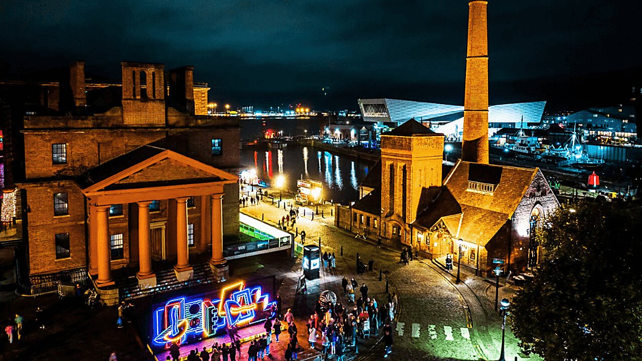 Part of the royal albert dock at night with a light installation on the front.