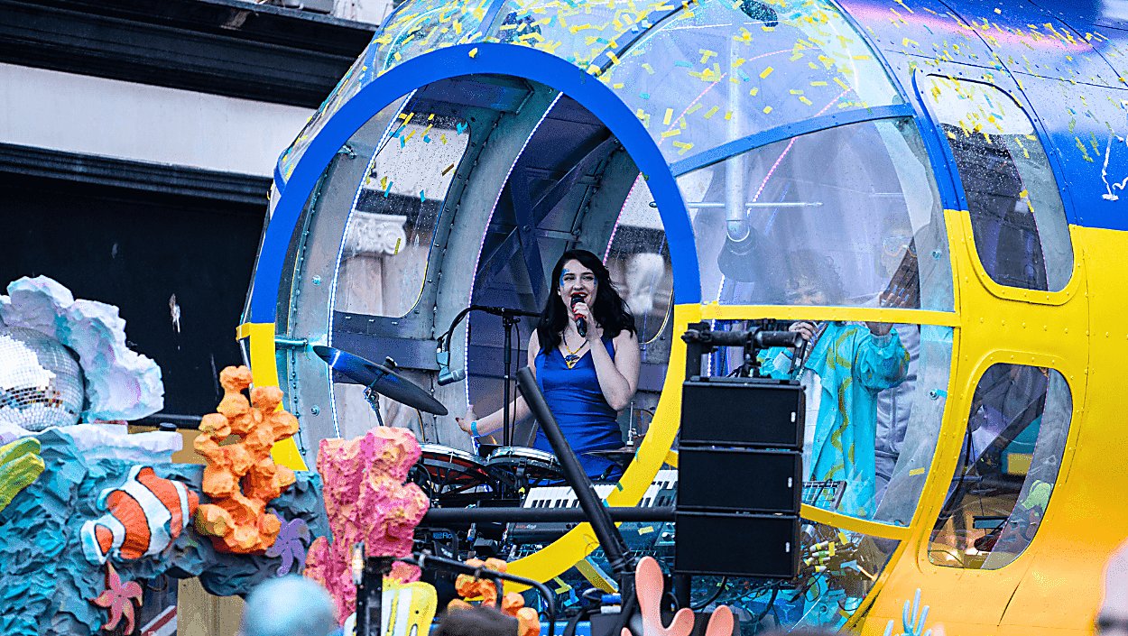 A lady dressed in a blue dress singing inside a large blue and yellow submarine