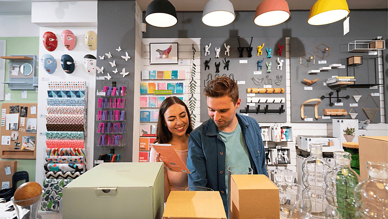 A young woman and male in their mid twenties are browsing amongst colourful homeware pieces and 'nick naks' in a quirky store.