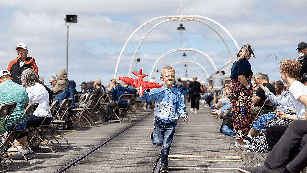A young boy running along the Southport Traditional Pier. They are holding a blow up aeroplane