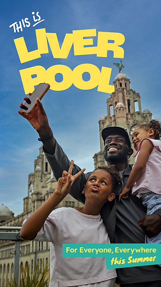 A family of three with one adult and two children taking a selfie infront of the Royal Liver Building. The text says 'This is Liverpool' in yellow text.