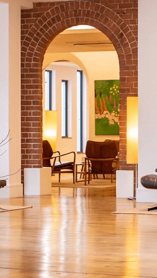 A modern, light lobby space with white walls, light oak flooring, an exposed brick archway and minimal decor and furnishings.