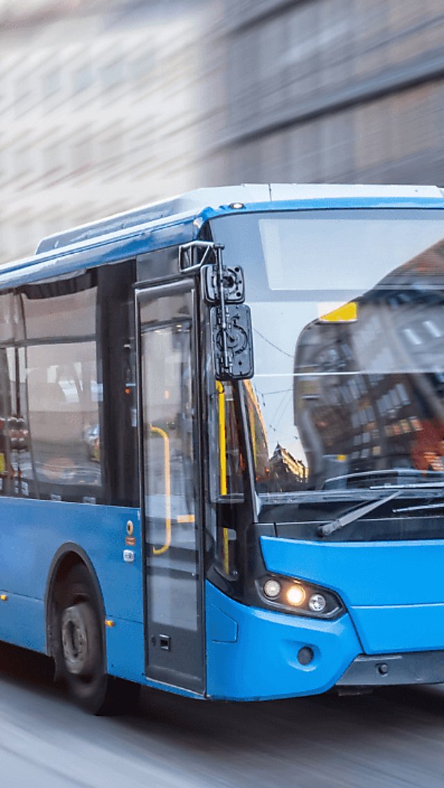 A turquoise coloured, single decker bus travelling through the city