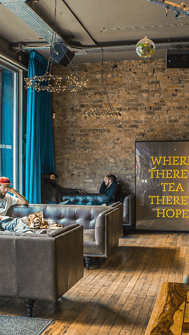 Inside the LEAF cafe. Against an exposed brick wall is a large print that reads 'where there's tea there's hope.' People are sitting at wooden tables and chairs in various chalky colours. There's also a disco ball hanging from the ceiling and a large red supporting column.