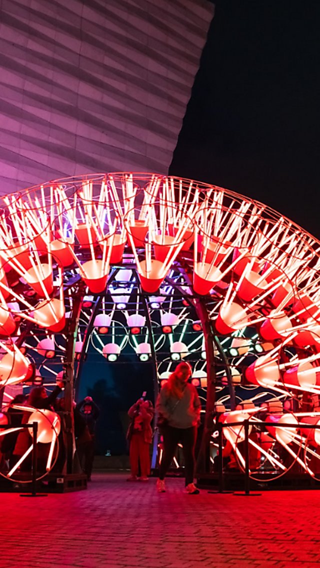 A large light installation that looks like a Dandelion lit up in red colours.