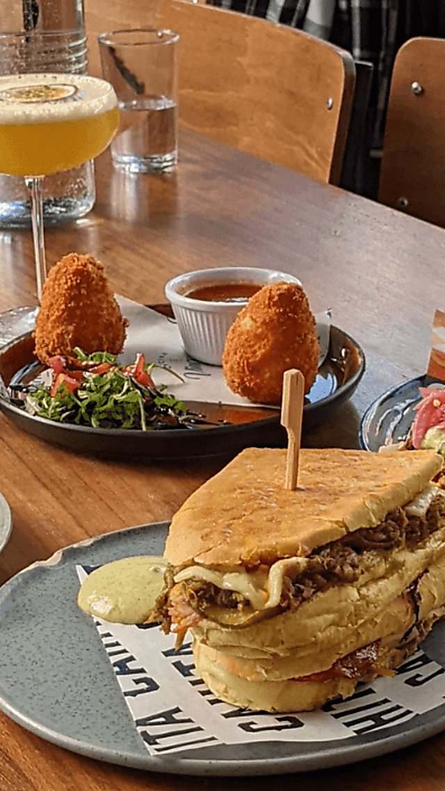 A selection of food on small, blue coloured plates from various street-food/restaurant vendors. Included is a cuban sandwich, Arancini, Tacos, Meatballs and Bruschetta. There's also a watermelon cocktail in a tall glass and a yellow, passionfruit cocktail in a Martini style glass.