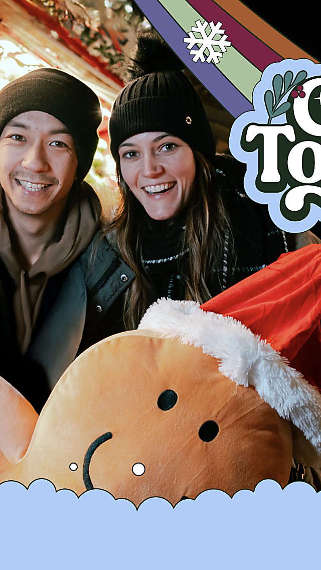 Two people at a Christmas market holding a large gingerbread man. There is a logo that says Get Together This Christmas.