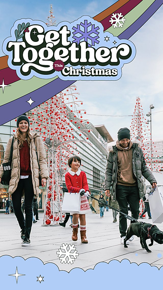 A family walking with their child and dog with Liverpool One Christmas trees behind them.