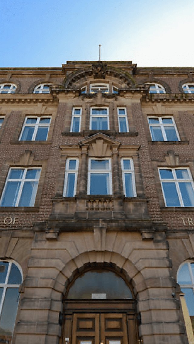 Outside an old sandstone coloured building with prominent doorway and large sash windows. The