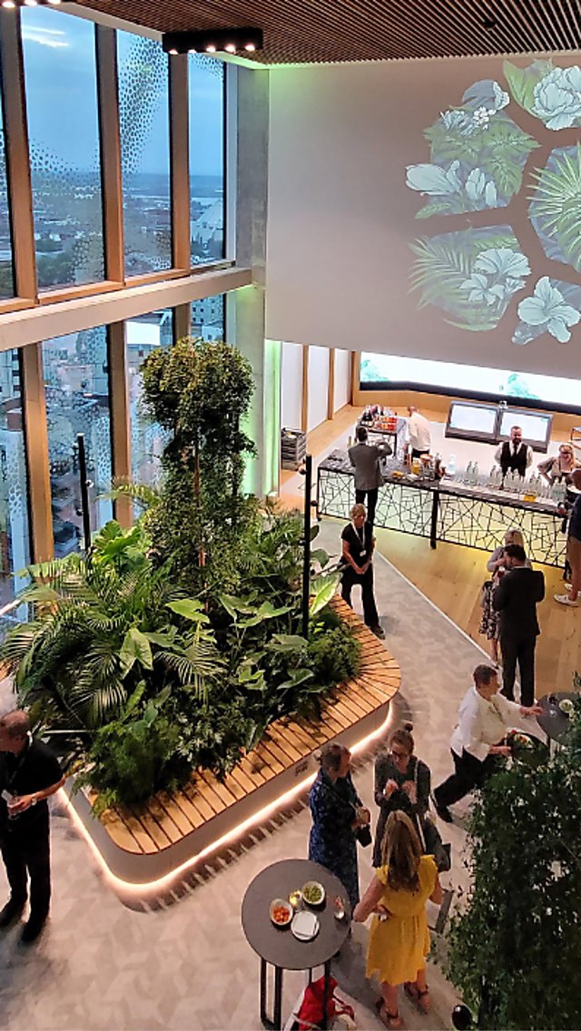 Event space in Spaces at The Spine with a lot of plants, green uplighters and a screen with a projection on it.