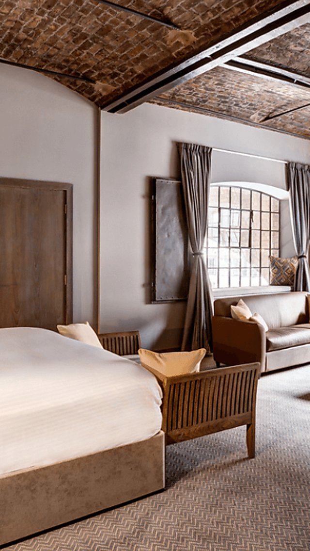 A hotel room with plush pillows and a large window with high ceilings.