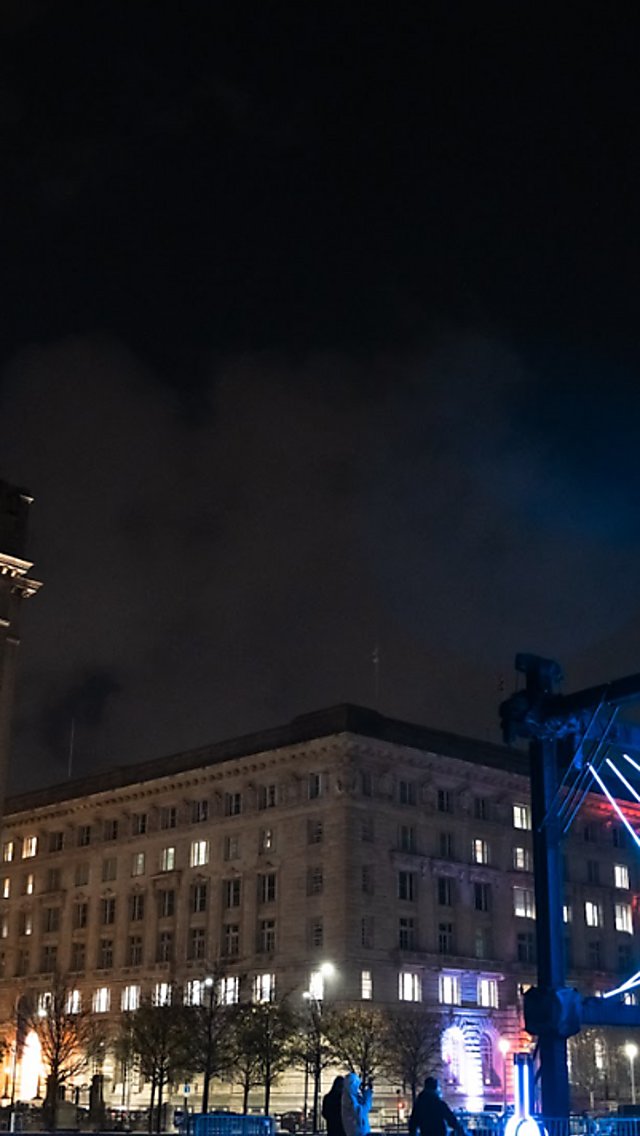 A large light installation that looks like a large pendulum outside of the Royal Liver Building.