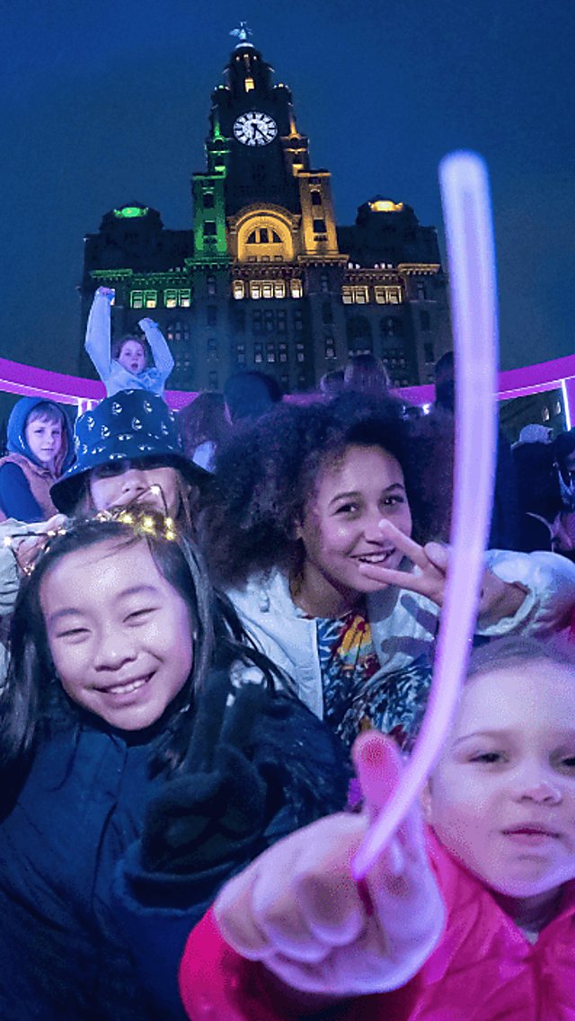 A group of children inside one of the light installations with the royal liver building in the background.