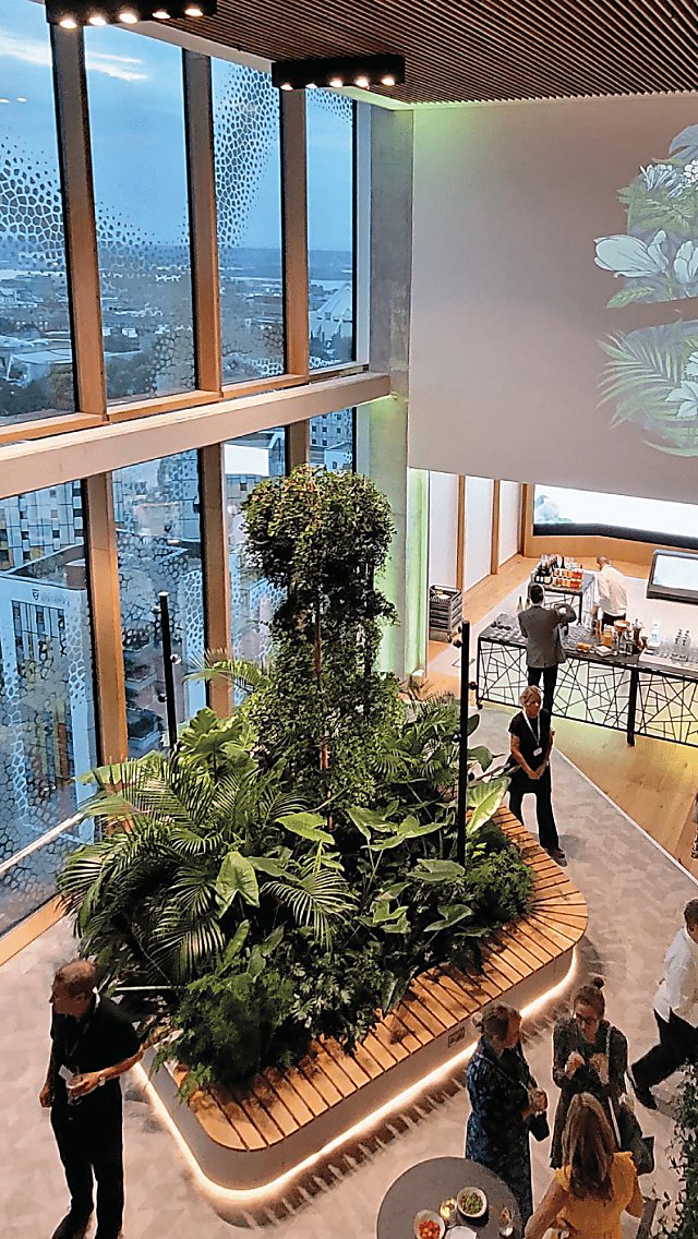 An image of people standing talking in a sustainable venue, there's flowers and other such foliage around them.