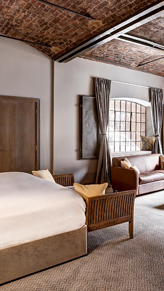 Inside a bedroom at the Titanic Hotel with a large vaulted ceiling rom, two large windows, a bed with two bedsid tables and a table and chairs. The ceiling is made of bricks.
