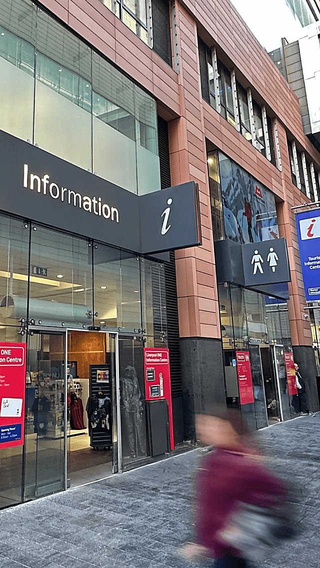 Liverpool Tourist Information Centre exterior image with people walking past the entrance. Outside there is a sign above the door which says 'Information' in silver writing.