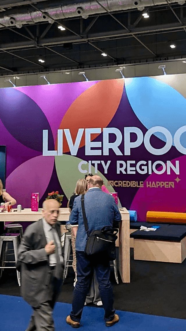 A Liverpool Convention Bureau stand with pink branding and a crowd of people standing talking.