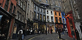 A street in Edinburgh with colourful shops outside, in yellow, blue and white.