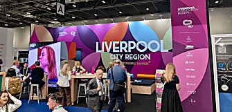 A Liverpool Convention Bureau stand with pink branding and a crowd of people standing talking.