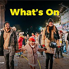 A family of three, two adults and a child walking through Christmas Markets in Liverpool at St George's Hall.