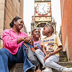Two children sitting with a woman with a large clock behind them.