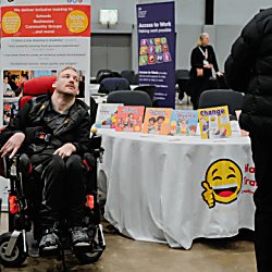 A wheelchair user sitting beside a table with a white tablecloth and a smiling face featured on the front of it.