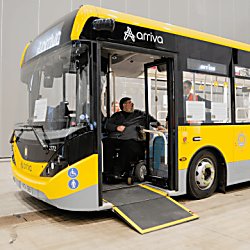 A yellow arriva bus with a man in a wheelchair sitting at the entrance of the bus.