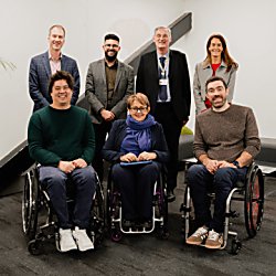 A group of seven people in a photo, three are in front and are wheelchair users with four able-bodied people standing behind them and smiling.